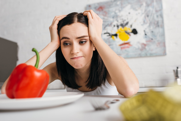 Selective focus of pensive woman looking at bell pepper near measuring tape on table - Photo, Image