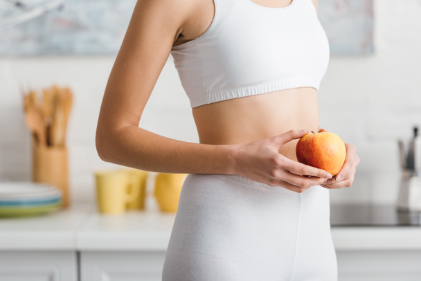 Cropped view of fit sportswoman holding fresh apple in kitchen  - Foto, Imagen