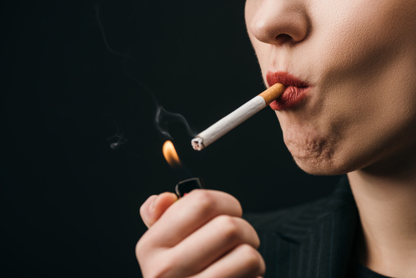 Vista cortada de mulher acendendo cigarro com isqueiro isolado em preto
  - Foto, Imagem