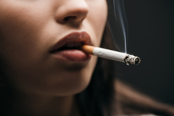 Selective focus of young woman smoking cigarette isolated on black  - Foto, afbeelding