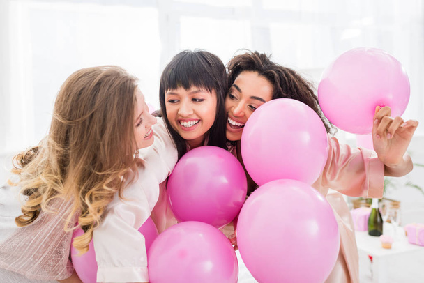 emotional multicultural girls having fun with pink balloons on pajama party - Foto, Imagem