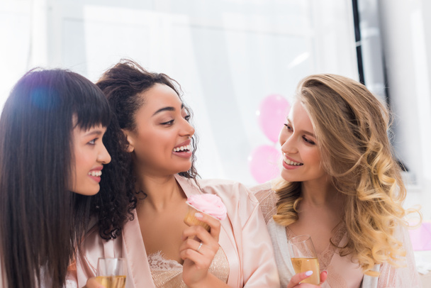 belles copines multiculturelles s'amuser avec champagne et cupcake pendant la fête de célibataire
  - Photo, image
