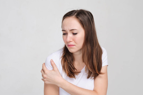 Una ragazza con una maglietta bianca si lubrifica la spalla con la mano. Il concetto di dolore muscolare
. - Foto, immagini