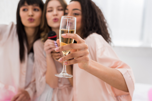 selective focus of champagne glass and singing girls on pajama party - Photo, Image