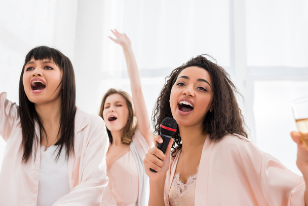 beautiful smiling multicultural girls singing with microphone on pajama party - 写真・画像