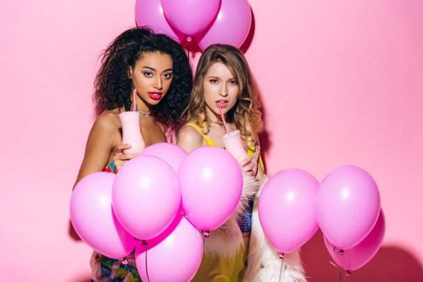 sexy multicultural girls drinking milkshakes on pink with balloons - Foto, immagini