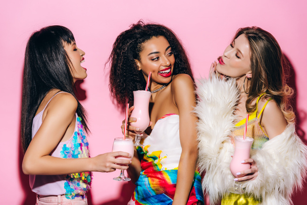 счастливые стильные мультиэтнические девушки, пьющие молочные коктейли на розовом
 - Фото, изображение