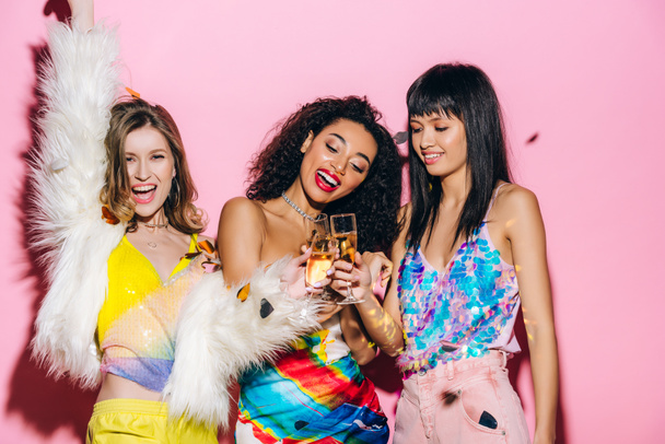 veselé multikulturní dívky baví s sklenicemi šampaňského na růžové s konfety - Fotografie, Obrázek