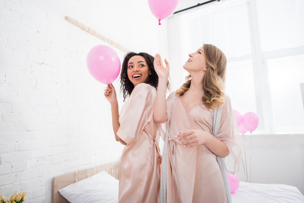 happy multiethnic girls in bathrobes holding pink balloons on bachelorette party - Photo, image