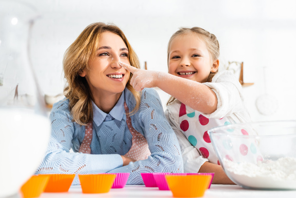 Selektivní zaměření dcery dotýkající se nosu matky při vaření v kuchyni - Fotografie, Obrázek