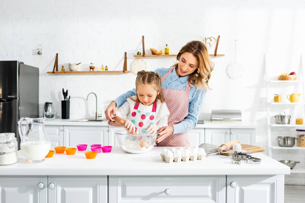 Beautiful attractive mother standing behind cute daughter while kneading dough - Photo, Image