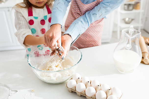 Обрізаний вид на матір і доньку, що замішує тісто в мисці на кухні
 - Фото, зображення