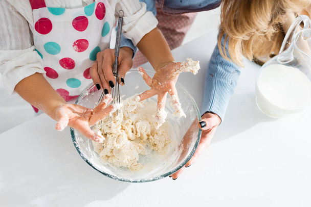 Vue recadrée des mains de l'enfant dans la pâte près de la mère tenant bol
 - Photo, image