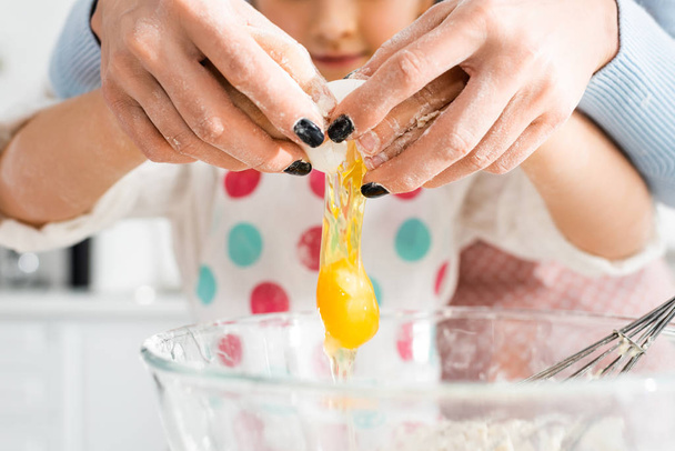 Selective focus of mother and daughter hands breaking egg over bowl together  - Φωτογραφία, εικόνα