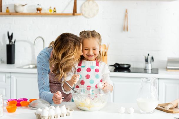 Mother and daughter smiling and happy during making dough for cupcakes together  - 写真・画像