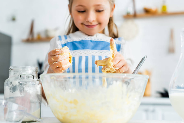 cropped view of smiling and cute kid in apron cooking dough in kitchen  - Foto, afbeelding