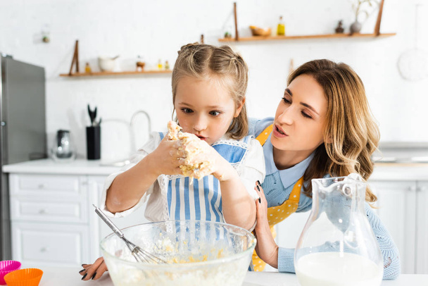 mother talking with shocked daughter during cooking dough  - Foto, Imagen