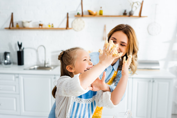 smiling mother and daughter with dough on hands playing in kitchen  - Фото, зображення