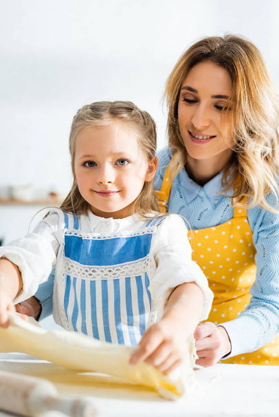 smiling mother looking at cute daughter with dough in kitchen  - Foto, imagen