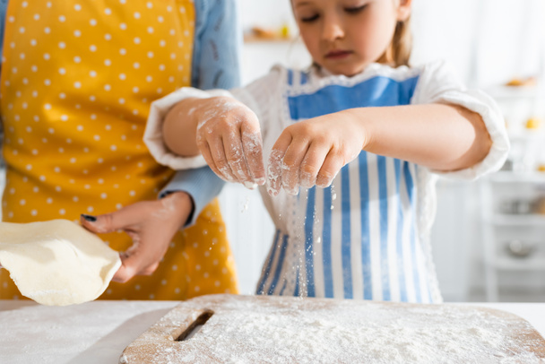 cropped view of mother holding dough and daughter sifting flour on cutting board  - Fotografie, Obrázek