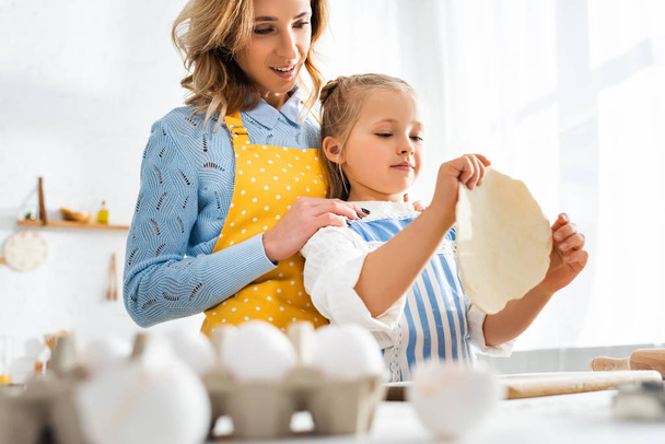 selective focus of mother looking at daughter with dough - Foto, Imagen