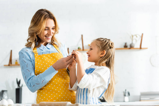 smiling mother and cute daughter holding dough mold in kitchen  - Foto, Imagem