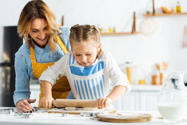 smiling mother and daughter cooking with rolling pin in kitchen  - Photo, image