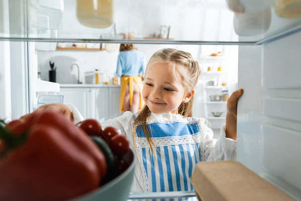 foco seletivo de sorrir filha olhando para legumes na geladeira
  - Foto, Imagem