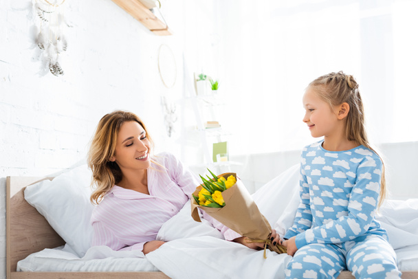 smiling daughter presenting bouquet to mother in mothers day - Fotoğraf, Görsel