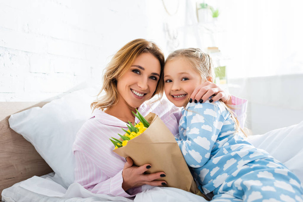 smiling mother with bouquet hugging daughter in mothers day - Photo, Image