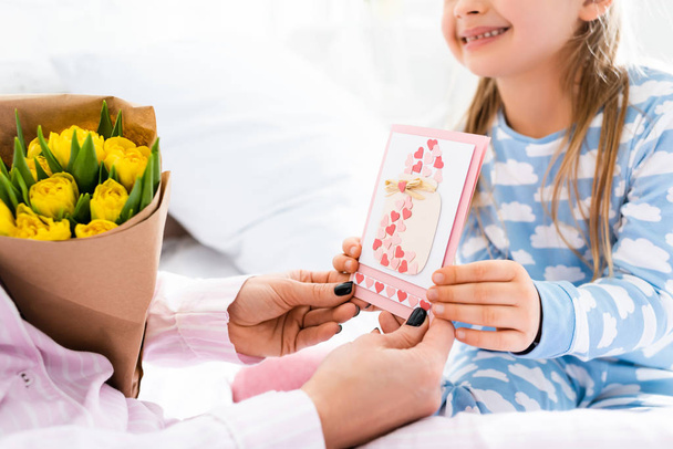 cropped view of smiling daughter giving card to mother in international womens day - 写真・画像