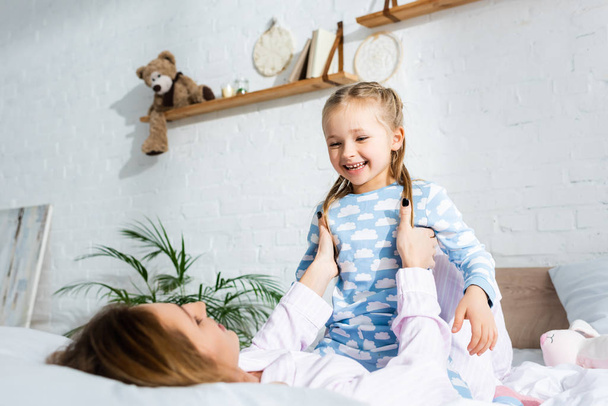 mother holding and playing with smiling daughter on bed   - Foto, Imagen
