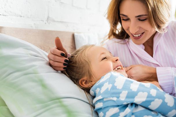 selective focus of smiling mother playing with daughter in bedroom  - Photo, Image