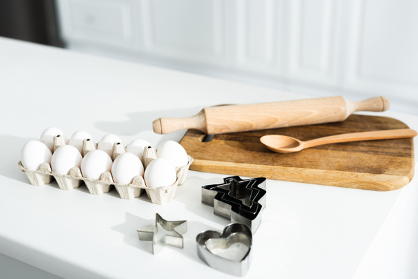 oeufs, planche à découper, cuillère, moules à pâte et rouleau à pâtisserie sur table
  - Photo, image
