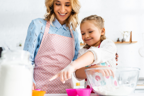 low angle view of smiling mother and daughter pointing with finger at dough mold - Foto, Bild