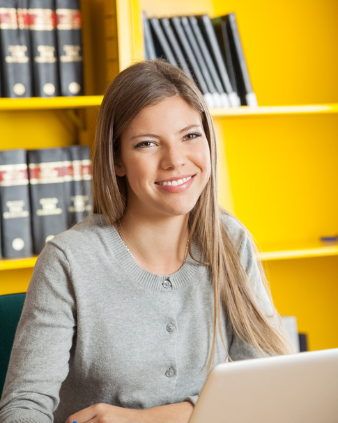 Student With Laptop Smiling Against Bookshelf In College Library - Foto, afbeelding