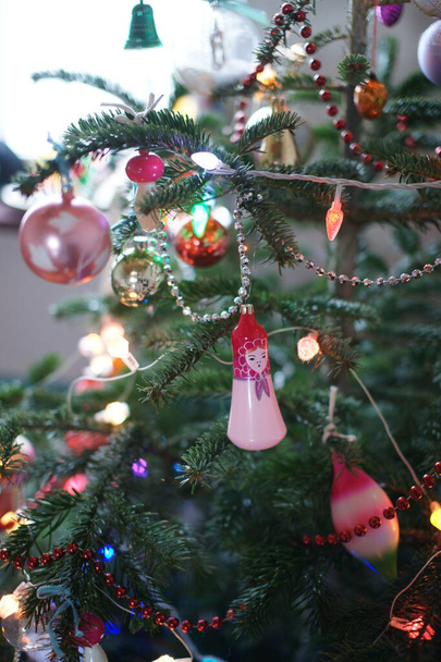 colored toys and garlands and ribbons on green fir tree in room background - Foto, afbeelding