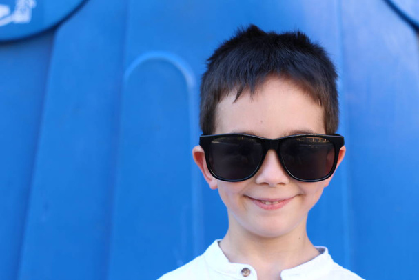 Außenporträt eines niedlichen Jungen mit großer Sonnenbrille auf blauem Hintergrund - Foto, Bild