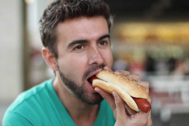 Zbliżenie portret przystojnego młodego mężczyzny jedzącego hot-doga  - Zdjęcie, obraz
