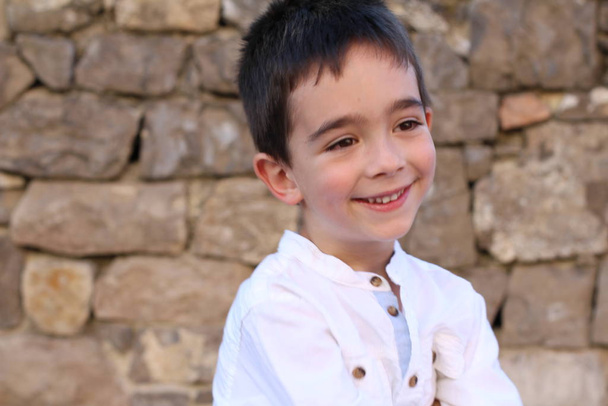 Κοντινό πλάνο πορτρέτο του χαριτωμένο μικρό αγόρι στέκεται σε τούβλο τοίχο φόντο  - Φωτογραφία, εικόνα