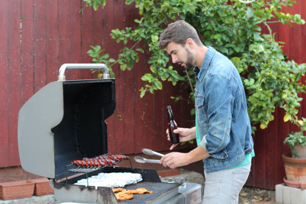 Outdoor portrait of young bearded man cooking food on BBQ in garden at daytime  - Foto, immagini