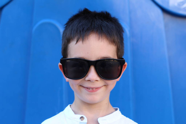 Outdoor portrait of cute child boy in big sunglasses on blue background - Photo, Image