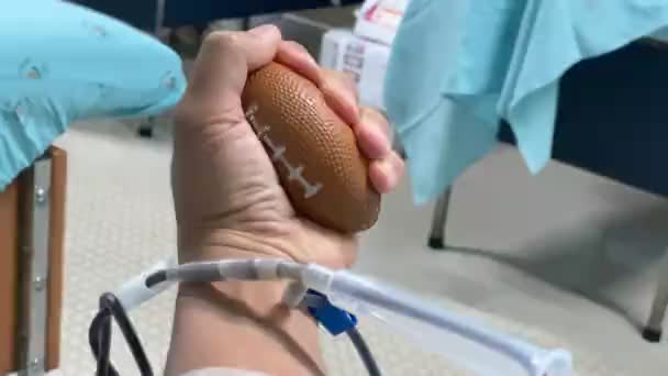 Ένα άτομο σφίγγει μια μπάλα ενώ αιμοδοσία σε κέντρο μετάγγισης. - Πλάνα, βίντεο