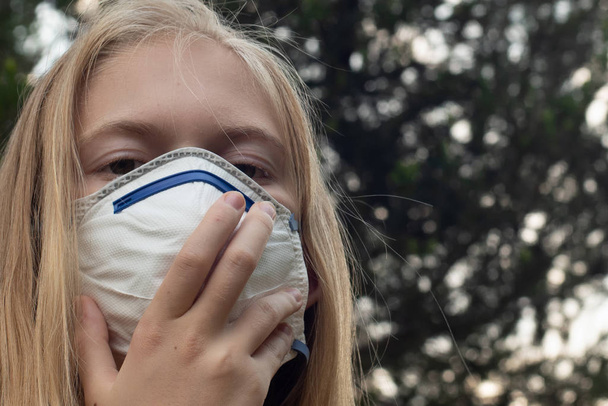 Menina loira usando P2 N95 proteção máscara respiratória para reduzir a quantidade de partículas respiratórias PM2.5
 - Foto, Imagem