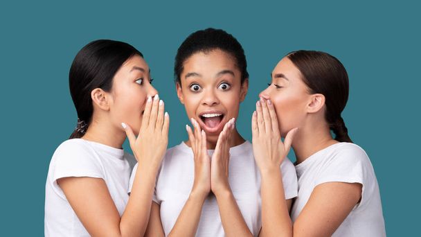 Drie meisjes fluisteren geheim nieuws staande op turquoise achtergrond, Panorama - Foto, afbeelding