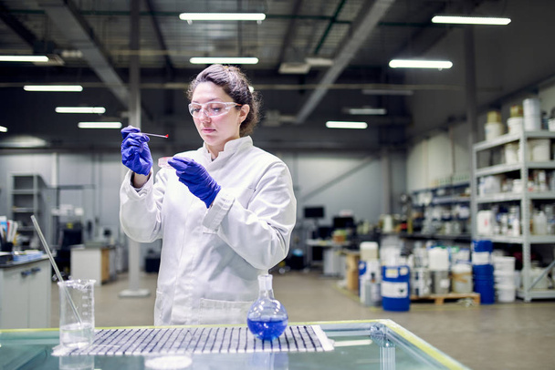 Серьезная лаборантка в белом халате с экспериментальным стеклом в руках проводит эксперименты
 - Фото, изображение