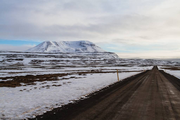 A road surrounded by the field and rocks covered in the snow under a cloudy sky in Iceland - Foto, Bild