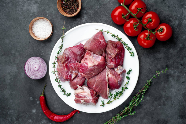 fresh sliced ??raw beef meat in a white bowl on a stone background with tomatoes and spices - Foto, Bild