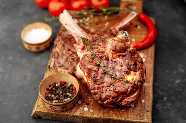 grilled beef steaks - tomahawk with tomatoes and red pepper on a stone background - Photo, Image