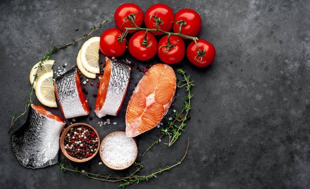 fresh raw salmon steaks and salmon tail on a stone background with salt, pepper, tomatoes, lemon with copy space for your text - Foto, Bild